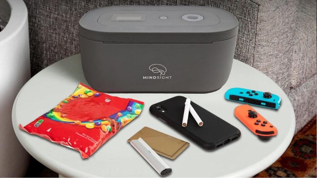 A person placing their smartphone into a Mindsight timed lock box on a wooden desk to improve focus.